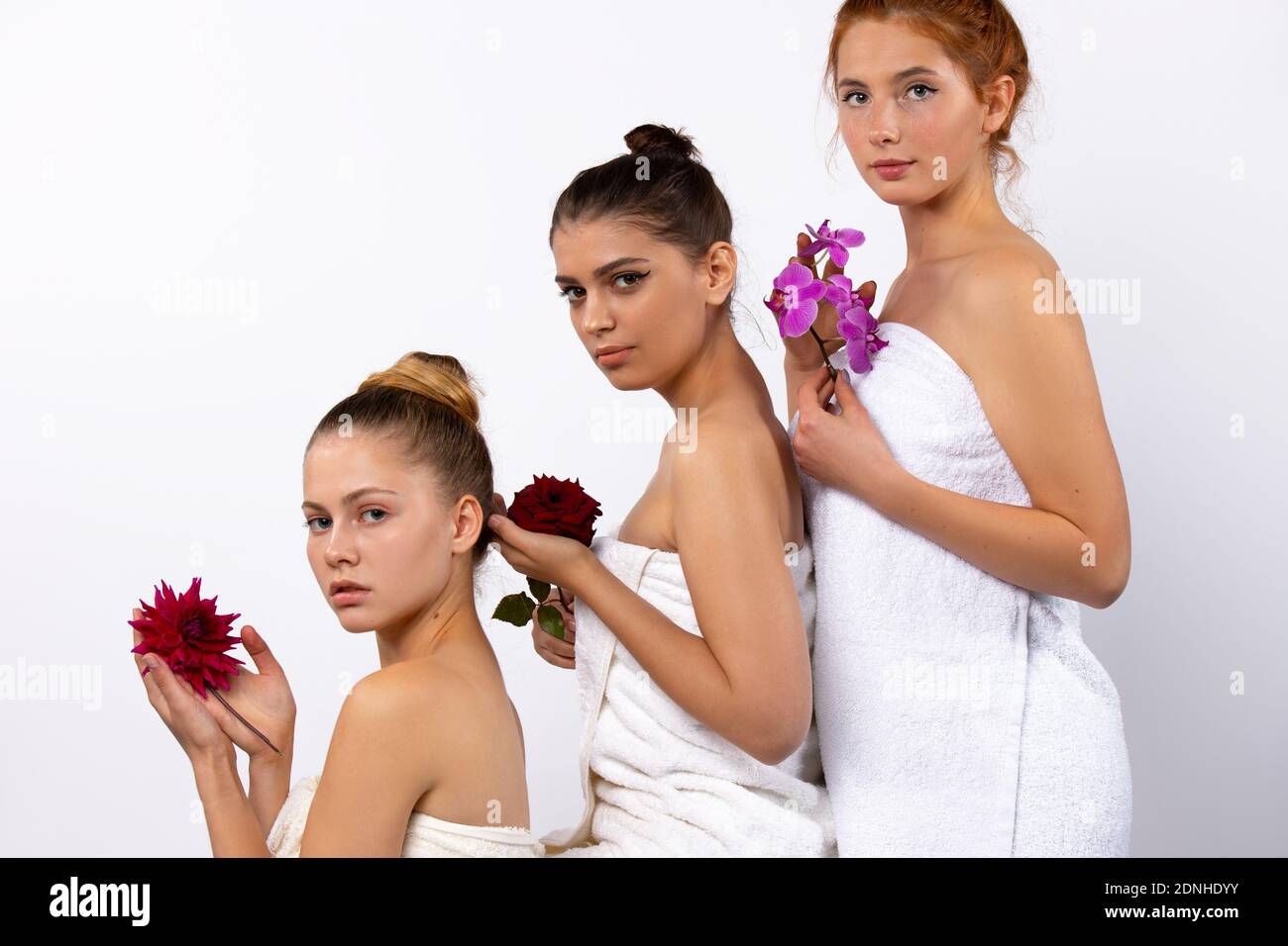 Spa-Modell Mädchen sind in weißen Handtüchern gewickelt und halten natürliche Blumen. Posiert in Form von Pyramide auf weißem Hintergrund. Stockfoto