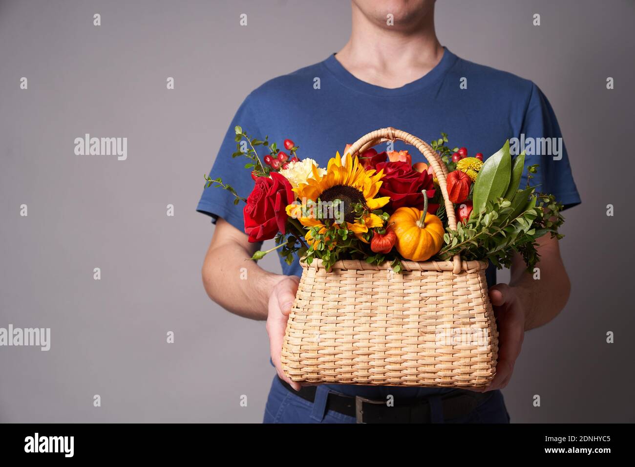 Ein weißer Mann in einem blauen T-Shirt hält einen Blumenkorb mit einem Kopierplatz auf einem grauen Hintergrund aus, Blumenlieferung Stockfoto
