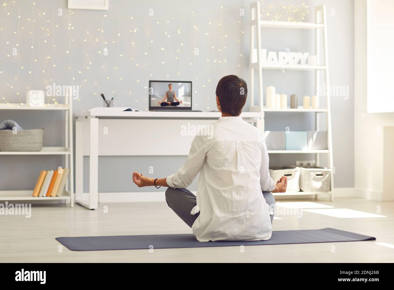 Frau sitzt auf Fitness-Teppich und praktiziert Meditation oder Yoga Online über Laptop Stockfoto