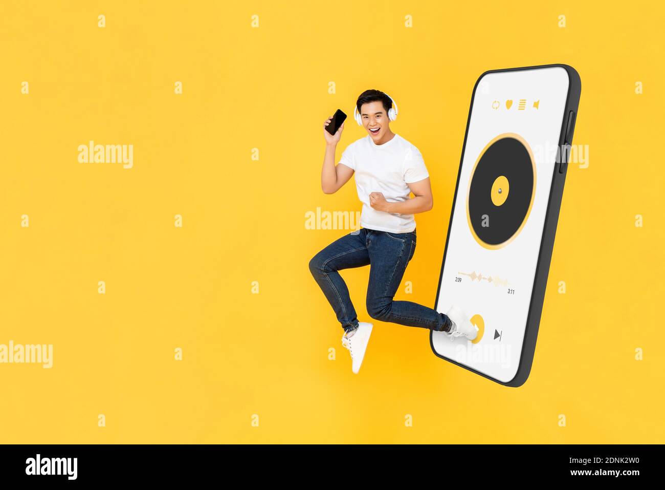 Glücklicher junger asiatischer Mann trägt Kopfhörer und hört Musik von Handy-Anwendung und Springen auf gelben Studio-Hintergrund mit Speicherplatz kopieren Stockfoto