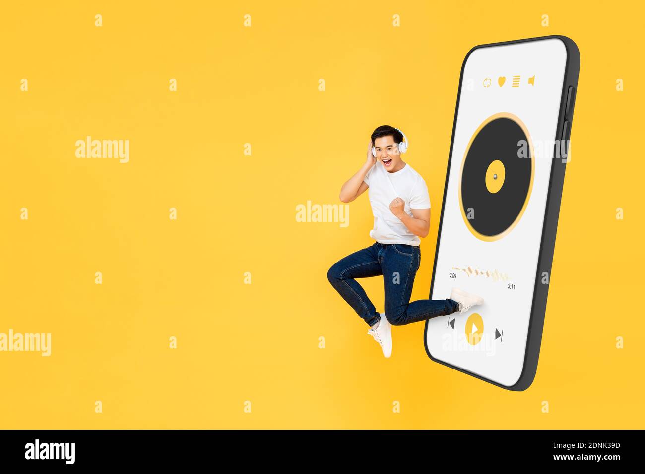 Glücklicher junger asiatischer Mann trägt Kopfhörer und hört Musik von Handy-Anwendung und Springen auf gelben Studio-Hintergrund mit Speicherplatz kopieren Stockfoto