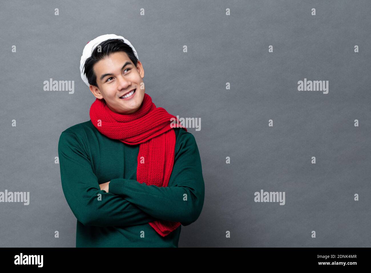 Junge schöne asiatische Mann in grün Weihnachten Pullover lächelnd und Blick auf den Kopierraum mit verschränkten Armen isoliert auf Grauer Hintergrund Stockfoto