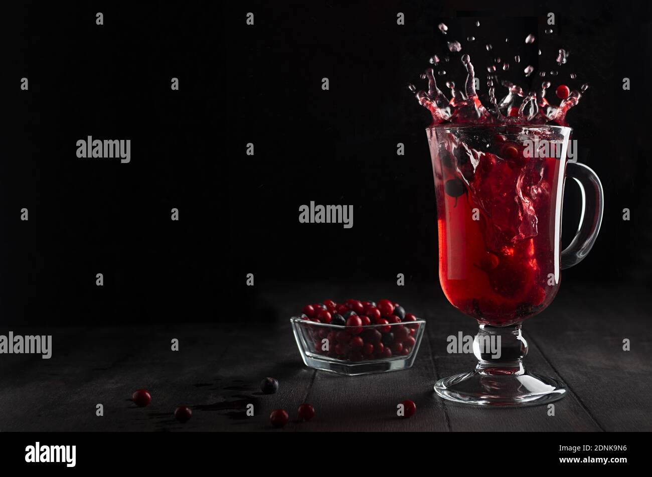 Leuchtend roter Glühwein mit Beeren und Spritzer in Glas Weinglas auf schwarzem Holztisch im dunklen Innenraum, Kopierraum. Stockfoto
