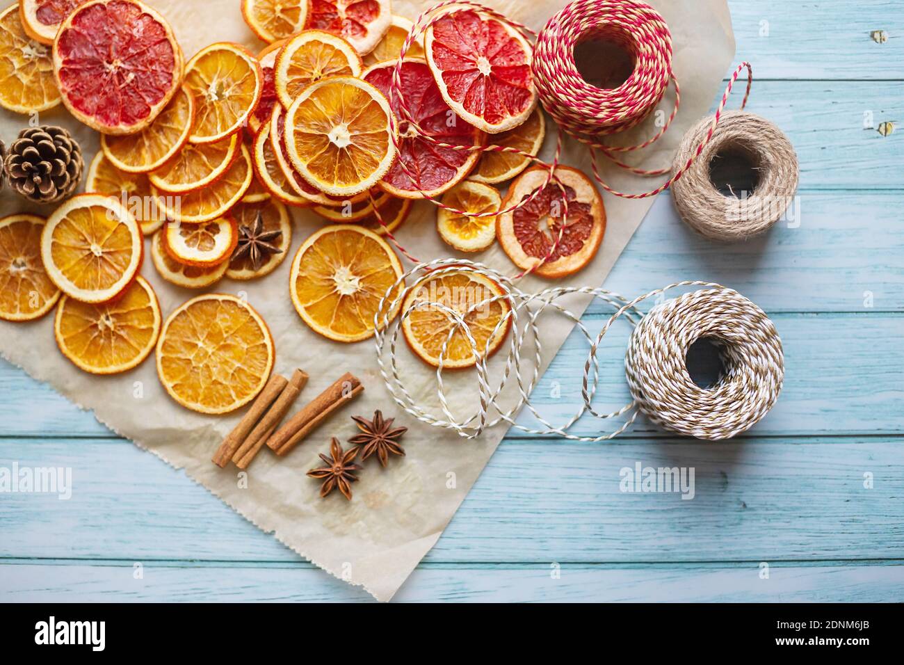 Zimt, Anis, getrocknete Orangen und Grapefruitscheiben, Fäden für diy-Projekte, Geschenkverpackung und schöne Öko-Weihnachtsdekorationen wie Kränze auf einem blauen Holztisch angeordnet Stockfoto