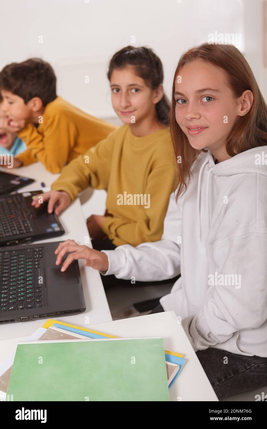 Vertikale Aufnahme von teen Mädchen Studenten lächeln an die Kamera Während der Arbeit an Computern in der Schule Stockfoto