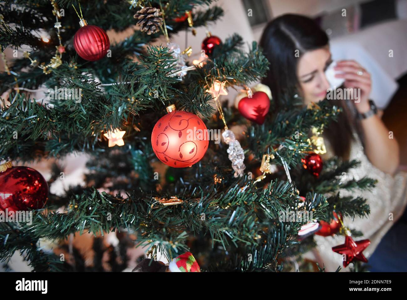 München, Deutschland. Dezember 2020. Themenbild Lonely Weihafteren 2020 in der Coronavirus-Pandemie. Eine junge Frau mit Gesichtsmaske, Maske sitzt allein hinter ihrem Weihaftertsbaum am Heiligabend und ist traurig, wischt Tränen aus den Augen, weint, weint, Pandemie, Lockdown, Shutdown, Inzidenzwert. MODELL FREIGEGEBEN! Quelle: dpa/Alamy Live News Stockfoto