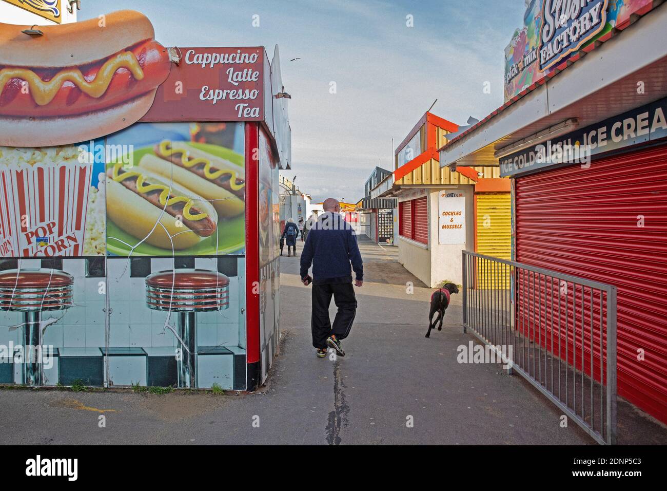 GROSSBRITANNIEN / Wales / Coney Beach Porthcawl / Mann mit Hund, der durch die Arkaden und den Vergnügungspark am Meer spaziert. Stockfoto
