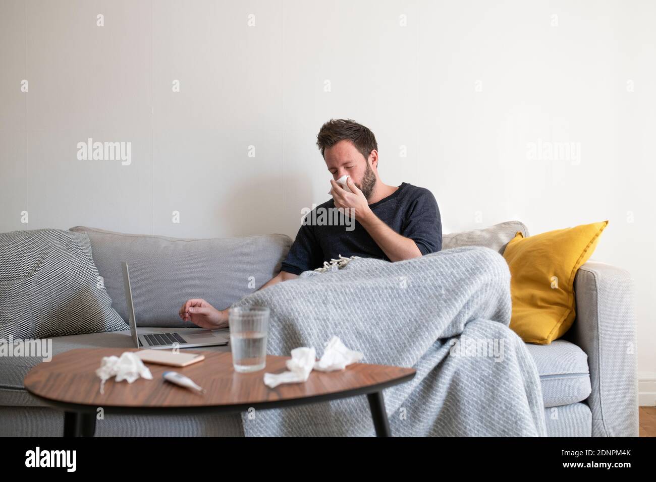 Kranker Mann auf dem Sofa mit Laptop Stockfoto