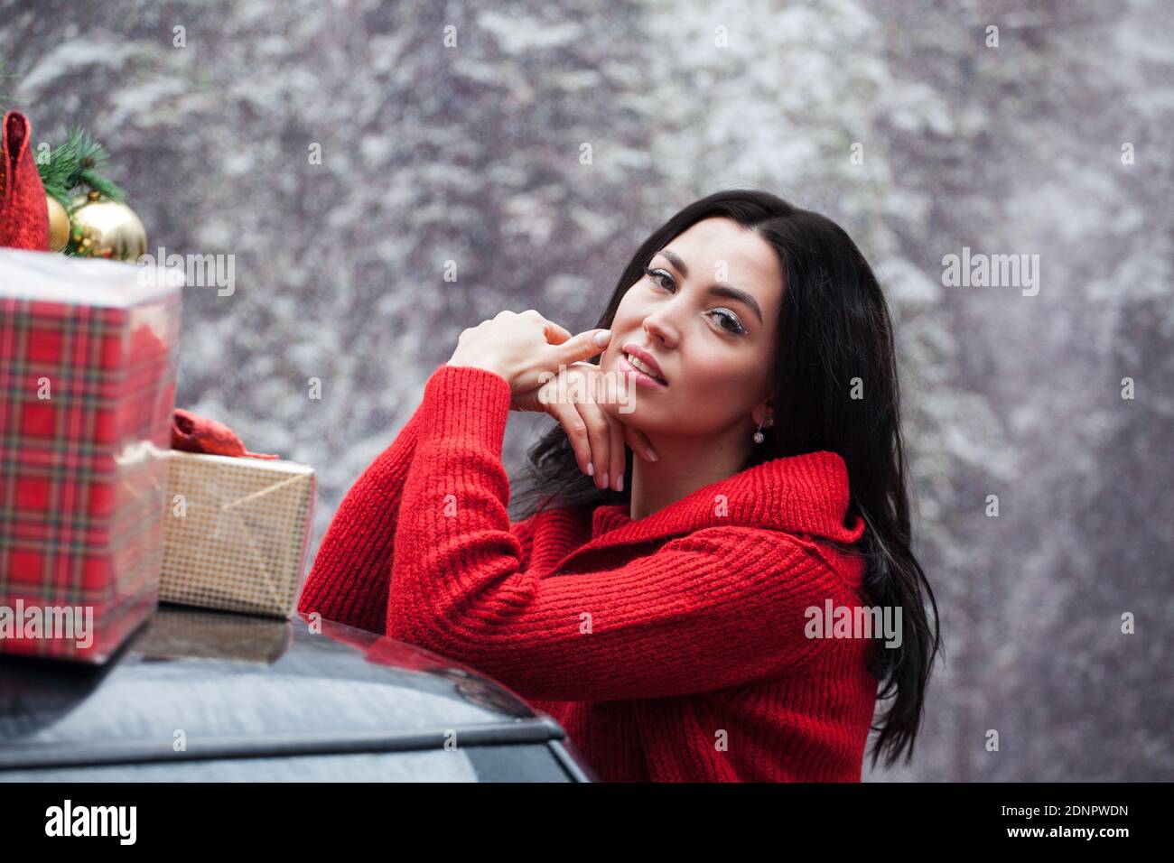 Portrait der glücklichen Frau in einem roten Pullover steht an einem roten Auto mit Neujahr Dekoration und Geschenke. Stockfoto