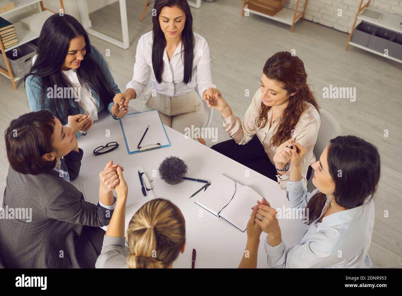 Gruppe von unterstützenden Business-Frauen sitzen um Bürotisch und Hände halten Stockfoto