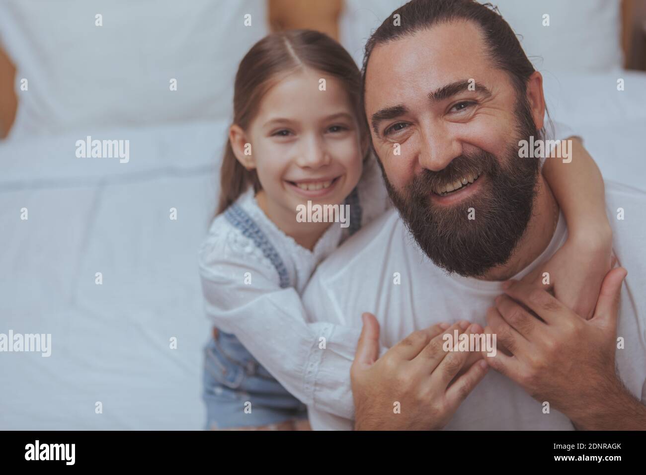 Nahaufnahme eines glücklichen alleinerziehenden Vaters und seiner niedlichen kleinen Tochter, die zur Kamera lächelt. Schönes kleines Mädchen umarmt ihren Vater, lächelnd freudig, kopieren Spa Stockfoto