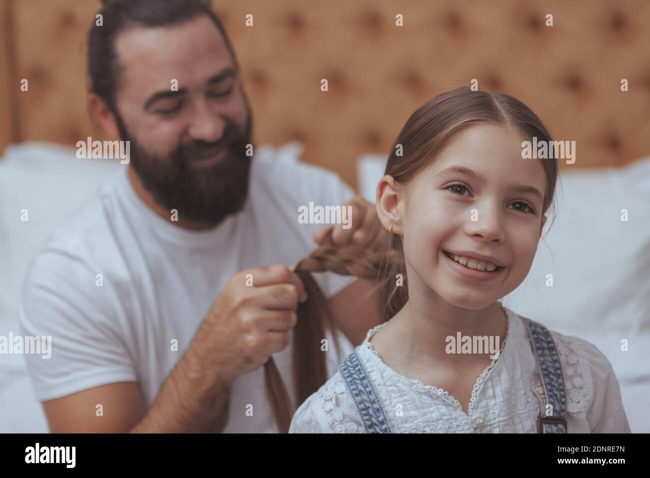 Nahaufnahme eines schönen glücklichen kleinen Mädchen lächelnd, Blick weg freudig, ihr Vater flechten ihre langen Haare auf dem Backgorund. Ledig gefleischte Väter Stockfoto