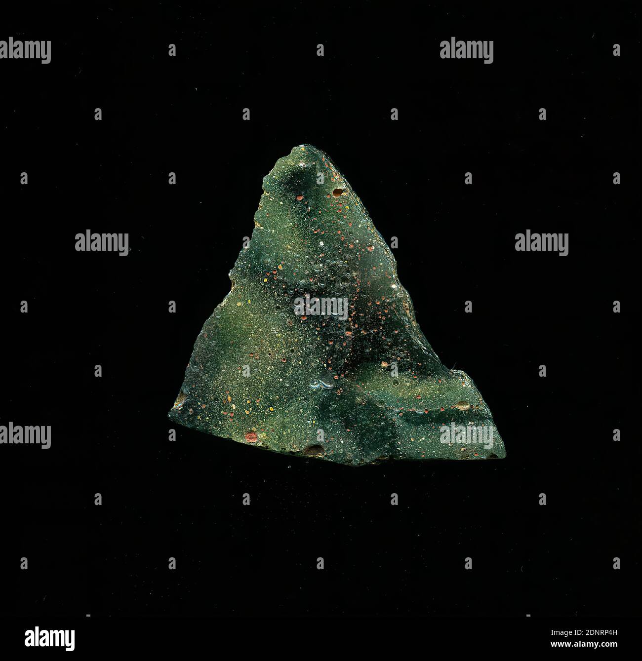 Mosaikglasfragment, Glas, gepresst, geschnitten, Gesamt: Höhe: 3.50 cm; Breite: 2.90 cm, Bodenbeläge, Wanddekoration, frühkaiserliche Zeit, das kleine Glasfragment zeigt einen unregelmäßigen Farbverlauf von mehreren hellen und dunkelgrünen Tönen. In der Römerzeit wurden farbige, verzierte Gläser für Gefäße, Mosaike, Wanddekorationen und Möbelschmuck verwendet. Für die Herstellung wurde verschiedenfarbiges Glas zu Rohren und Stäben geformt. Diese wurden zusammengedrückt und erhitzt, was zu einer langen Stange führte. Das Glas, jetzt in Scheiben geschnitten, hatte eine Vielzahl von amorphen oder floralen Mustern Stockfoto