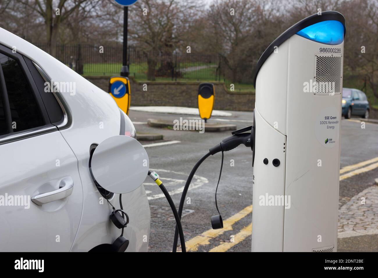 Dickes schwarzes Elektrokabel, das das weiße Elektroauto mit dem Ladepunkt an der Straße, Greenwich, London, verbindet Stockfoto