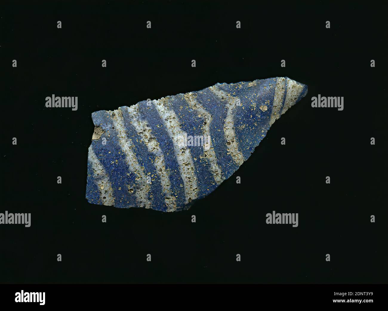 Fragment eines Gefäßes, Glas, gepresst, geschnitten, Gesamt: Höhe: 3.50 cm; Breite: 1.60 cm, Behälter, Lagerung, Küchenarbeit, frühkaiserliche Zeit, EINE leichte Krümmung des Glassfragments ermöglicht die Zuordnung zu einem Gefäß, möglicherweise einer Schüssel. Durch das blaue Glas verlaufen parallel weiße Linien. Auf der Rückseite sind zwei kleine weiße Punkte zu sehen. Für die Herstellung wurden verschiedenfarbige Gläser zu Rohren und Stäben geformt. Aufgrund des aufwendigen Herstellungsprozesses und seiner Zerbrechlichkeit galt Glas als eines der Luxusgegenstände der Antike Stockfoto
