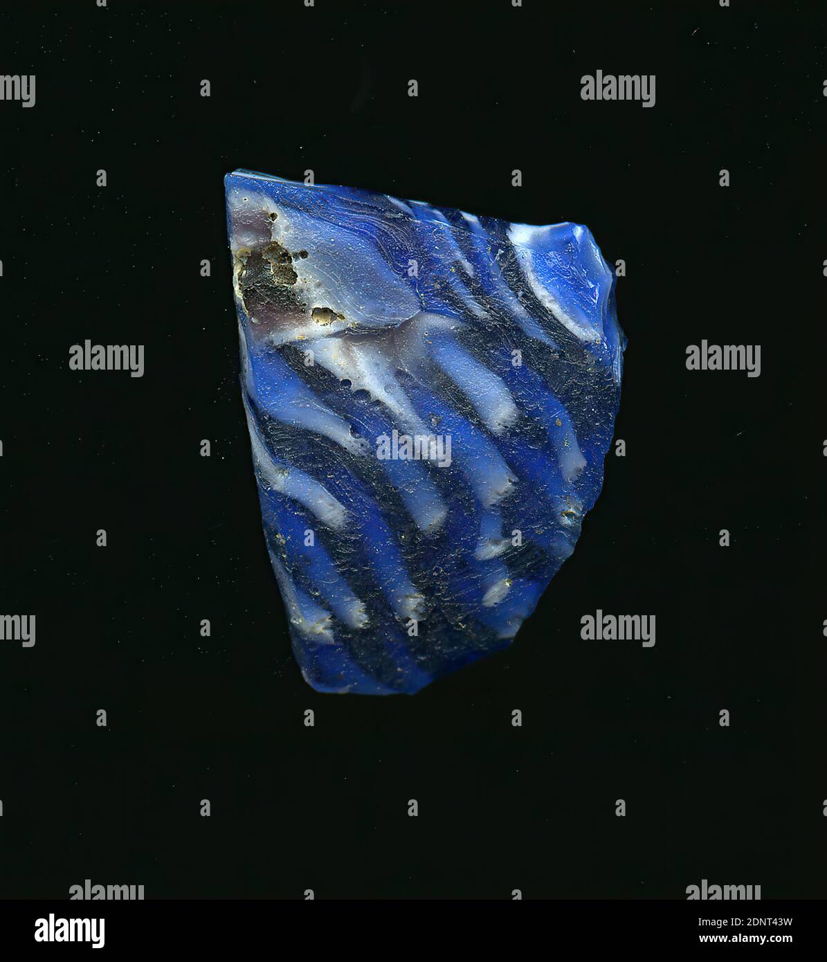 Fragment eines Gefäßes, Glas, gepresst, geschnitten, Gesamt: Höhe: 2,30 cm; Breite: 1,60 cm; Tiefe: 0,20 cm, Behälter, Lagerung, Küchenarbeit, frühkaiserliche Zeit, EINE leichte Krümmung des Glassfragmentes ermöglicht die Zuordnung zu einem Gefäß. Das blaue Glas ist mit mehreren weißen Punkten bedeckt, die verzogen sind. Für die Herstellung wurden verschiedenfarbige Gläser zu Rohren und Stäben geformt. Diese wurden zusammengedrückt und erhitzt, was zu einer langen Stange führte. Das in Scheiben geschnittene Glas hatte verschiedene amorphe oder florale Muster. Stockfoto
