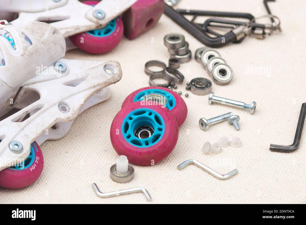 Austausch des Schlittschuhrollenlagers. Demontierte Rollschuhe, neue und verschlissene Lager, Achsen, Buchsen, Schrauben und Sechskantschlüssel. Stockfoto