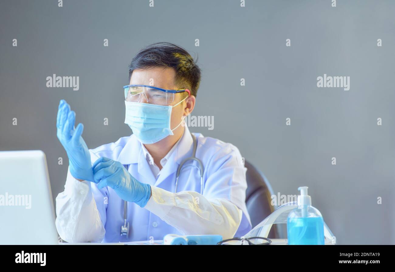 Porträt eines Arztes, der an seinem Schreibtisch sitzt und sich aufsetzt OP-Handschuhe Stockfoto