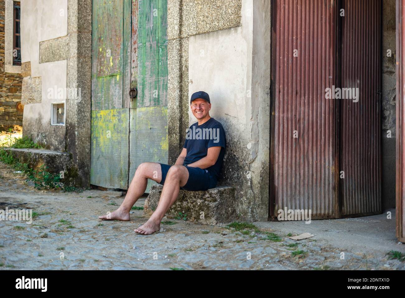 Portrait eines modernen Mannes, der vor einem alten ländlichen Gebäude sitzt Stockfoto