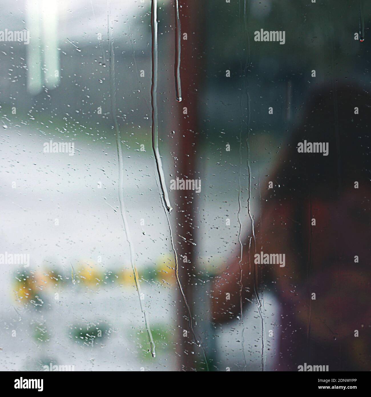 Regentropfen fließen durch das Glas, hinter dem Glas wird die Silhouette eines Mädchens vom Betrachter abgewandt Stockfoto