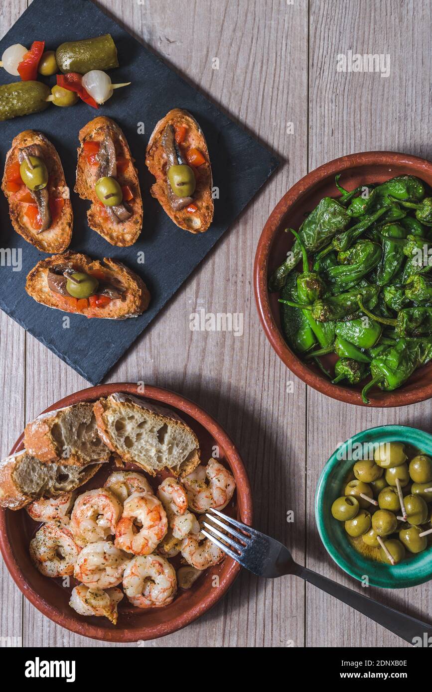 Obere vertikale Ansicht eines Holztisches mit Aufläufen mit Garnelen und grünen Paprika, ein Tablett mit kleinen Toasts mit rotem Pfeffer und Sardellen und vorbereitet Stockfoto