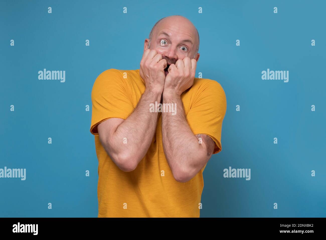 Reifer Mann, der den Mund mit Händen und runden Augen bedeckt und tiefes Staunen und Angst erlebt. Studio auf blauer Wand. Stockfoto