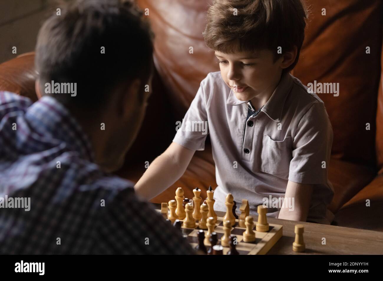 Aufmerksamer Junge Junior Schüler, der Schach mit jungen männlichen Trainer spielt Stockfoto