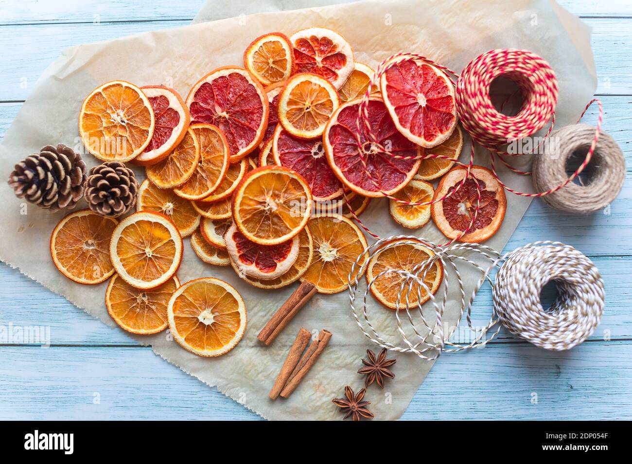 Zimt, Anis, getrocknete Orangen und Grapefruitscheiben, Fäden für diy-Projekte, Geschenkverpackung und schöne Öko-Weihnachtsdekorationen wie Kränze auf einem blauen Holztisch angeordnet Stockfoto