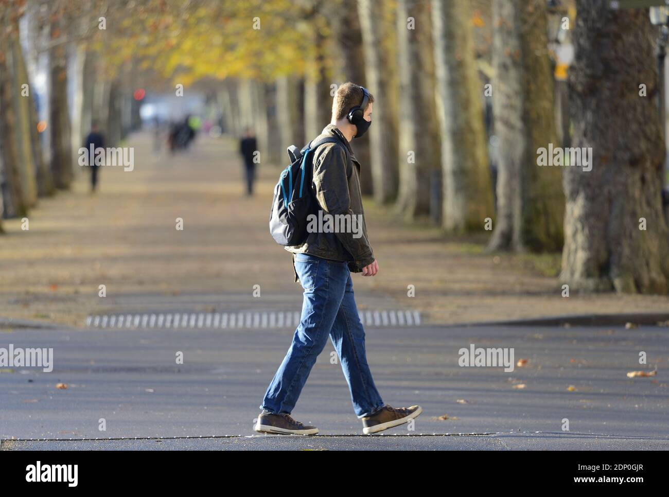 London, England, Großbritannien. Junger Mann mit Kopfhörern und Gesichtsmaske beim Spaziergang in der Mall, Dezember 2020 während der COVID-Pandemie Stockfoto