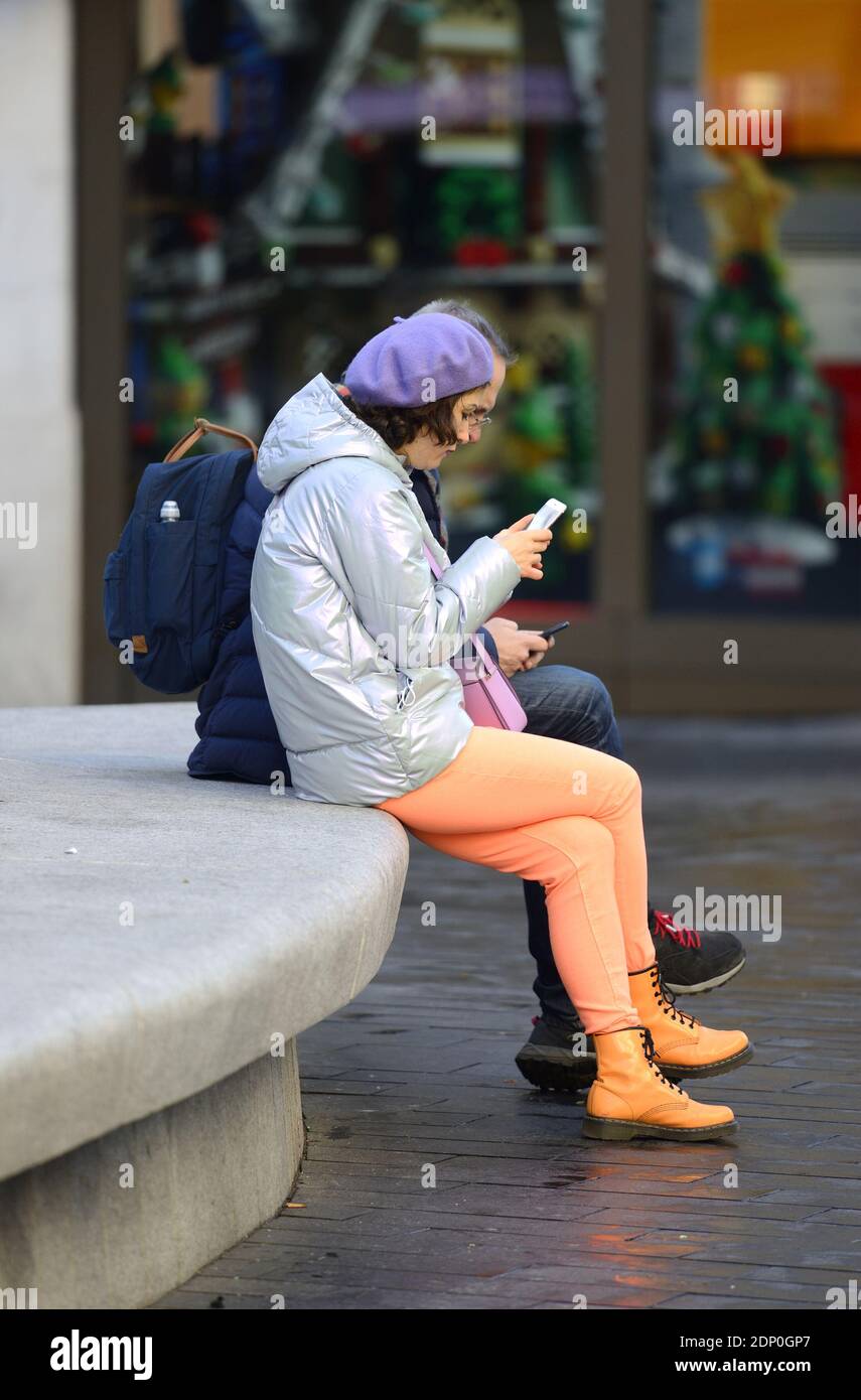 London, England, Großbritannien. Frau trägt leuchtend orange / Pfirsich Leggings und Turnschuhe, auf ihrem Handy in Leicester Square Stockfoto