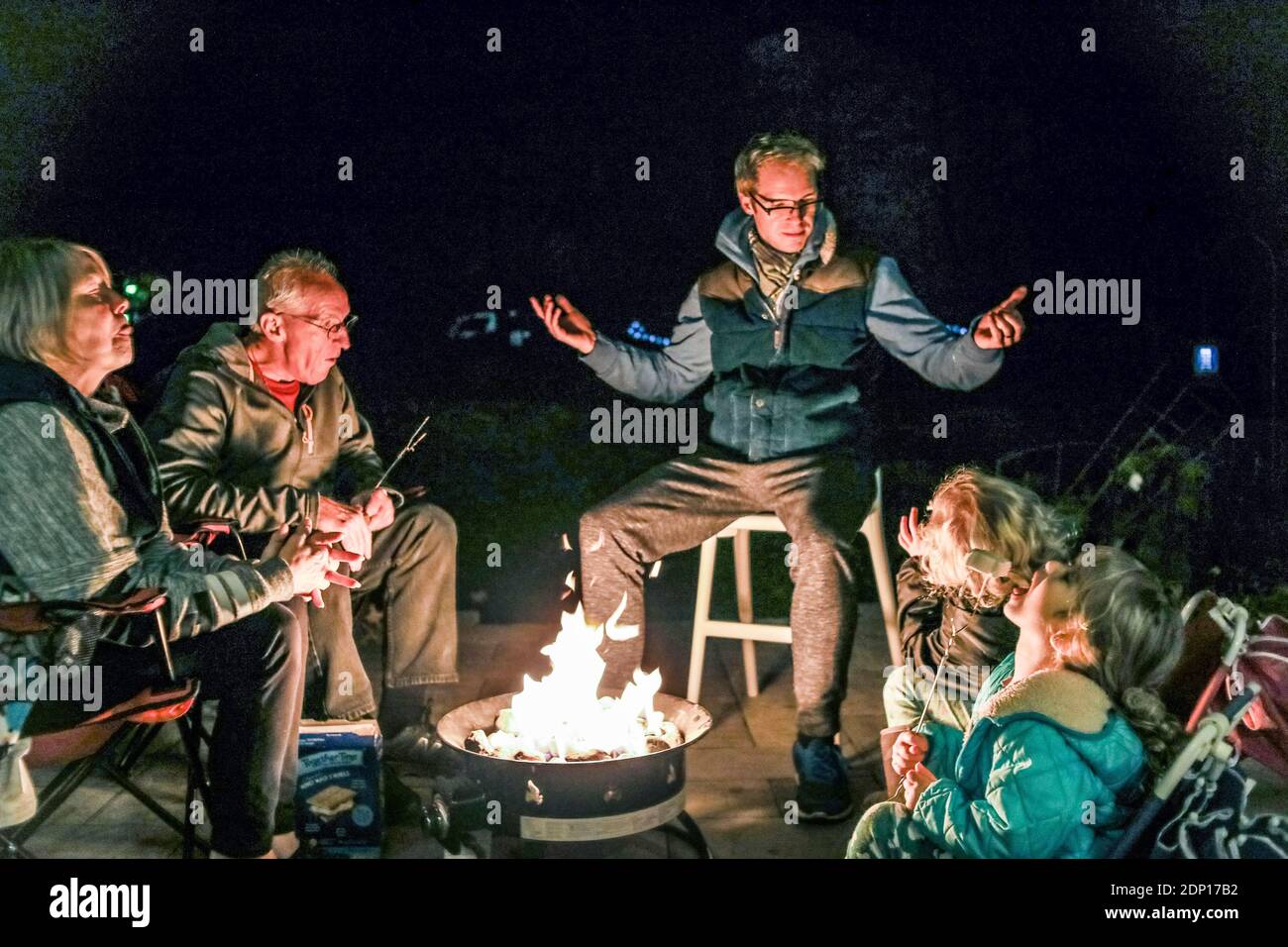 Familie versammelt sich um Feuerstelle draußen Geschichten erzählen und essen Stockfoto