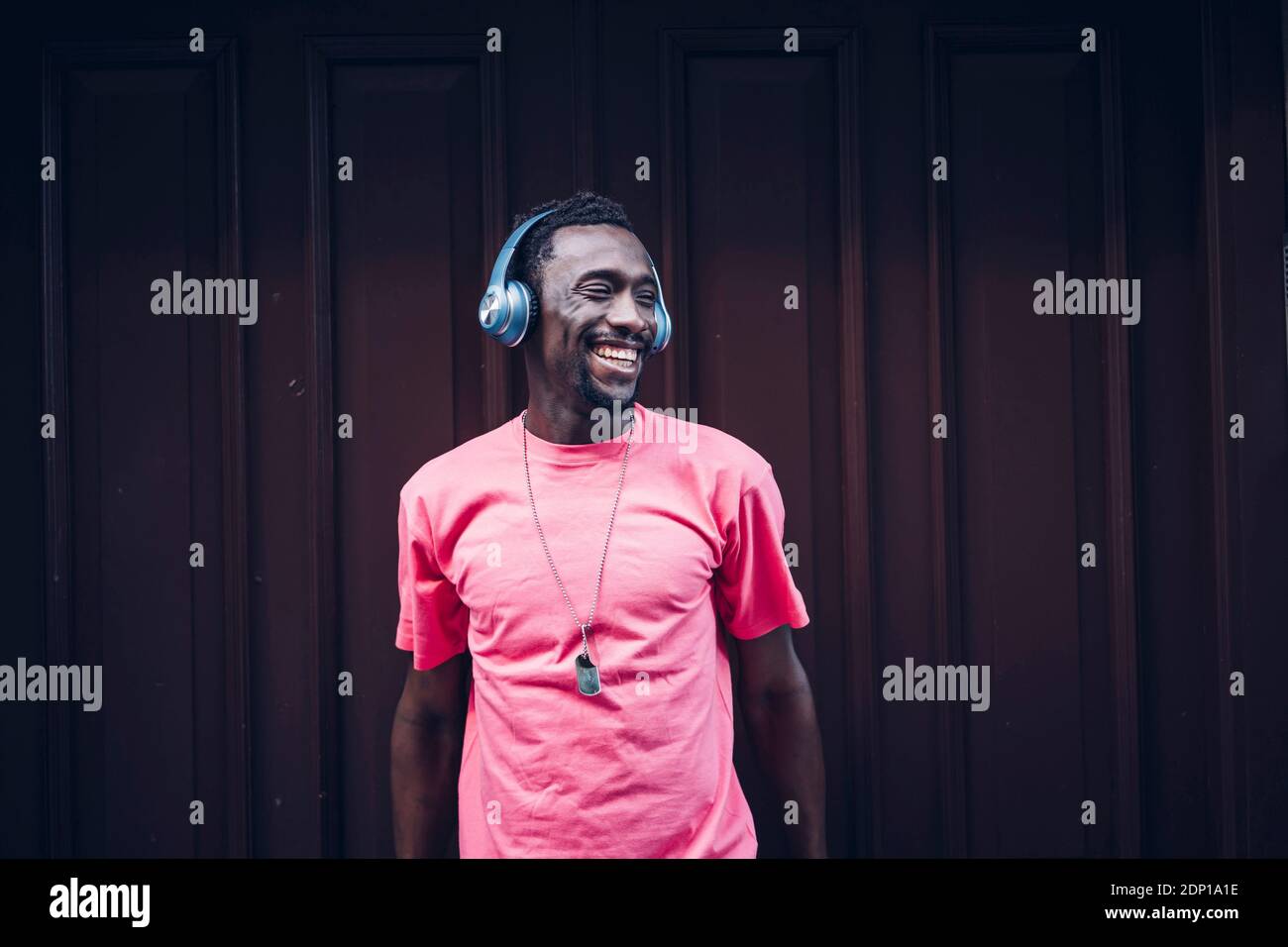 Lachender Mann mit pinkem T-Shirt, der mit Kopfhörern Musik hört Stockfoto