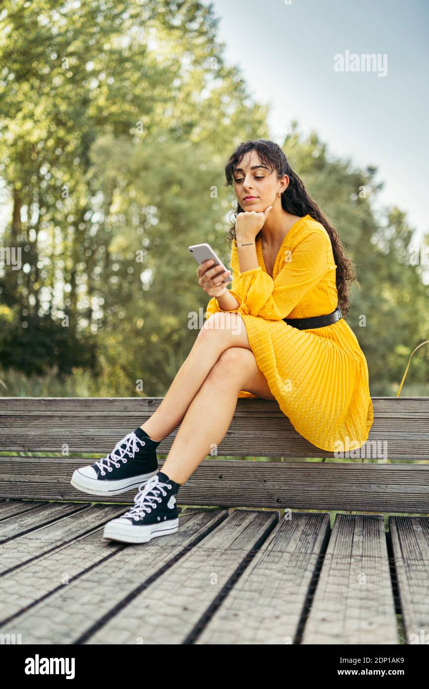 Junge Frau tragen gelbe Kleid und schwarze Turnschuhe und Sie ihr Smartphone auf hölzernen Boardwalk Stockfoto