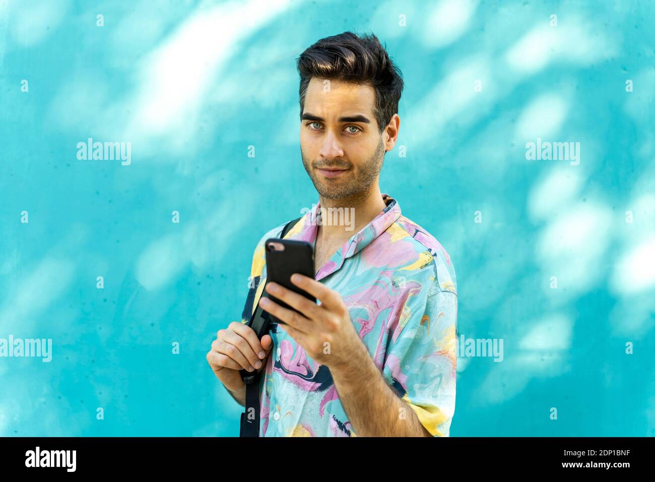 Dunkelhaariger Mann mit Smartphone vor der blauen Wand Stockfoto