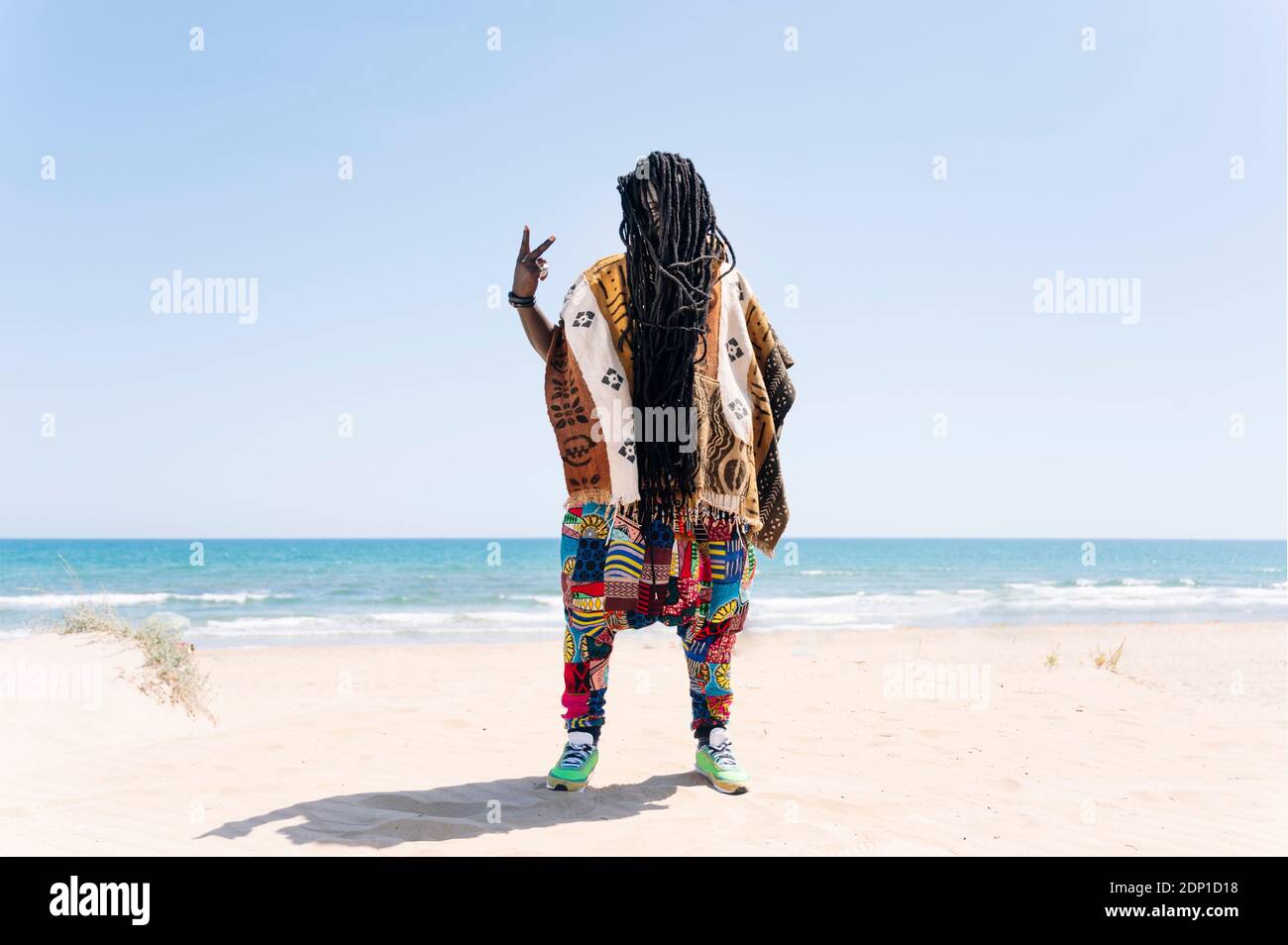 Mann, der am Strand steht und Dreadlocks sein Gesicht versteckt und unhöfliche Handzeichen macht Stockfoto