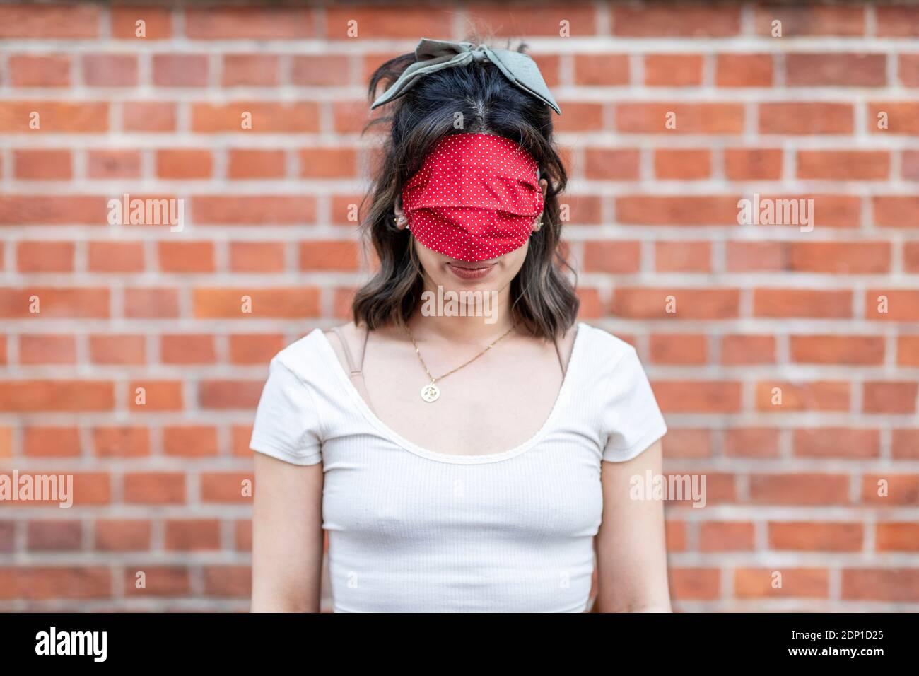 Nahaufnahme des Gesichts einer jungen Frau, bedeckt mit roter Maske im Stehen Gegen Backsteinmauer in der Stadt Stockfoto