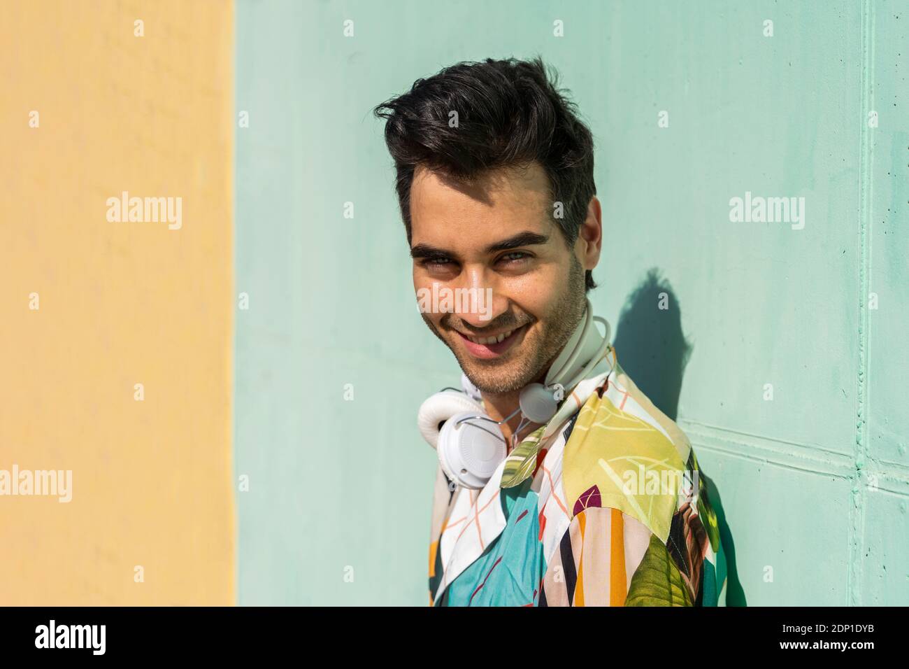 Dunkelhaariger Mann, der vor einer farbenfrohen Wand steht und lächelt Stockfoto