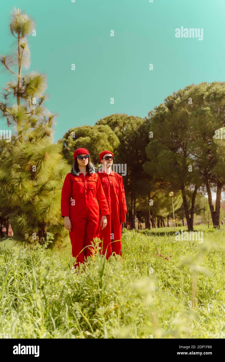 Junges Paar trägt rote Overalls und Hüte stehen auf einem Wiese in der Ferne Stockfoto