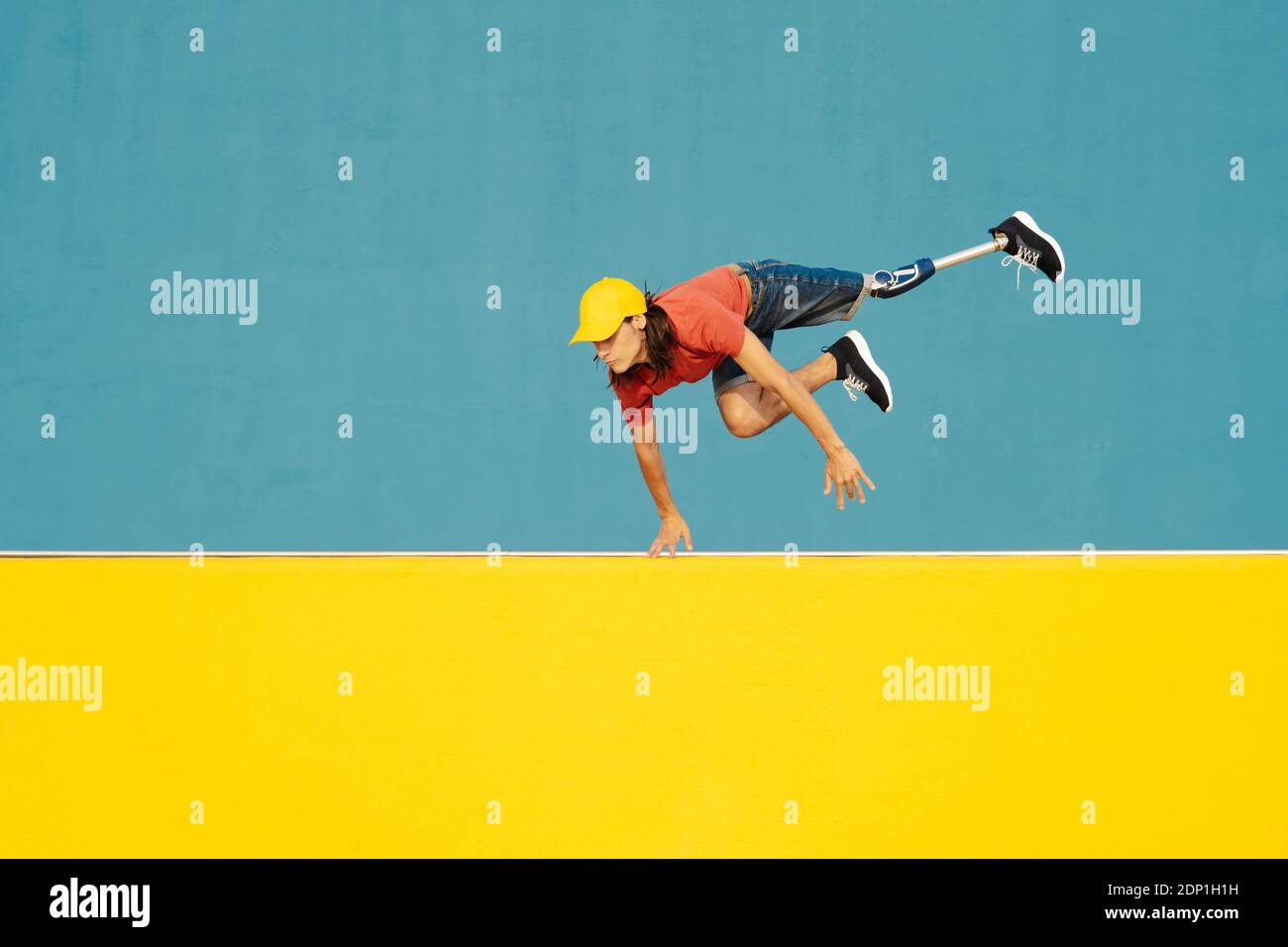 Mann mit körperlicher Behinderung springt gegen mehrfarbige Wand Stockfoto