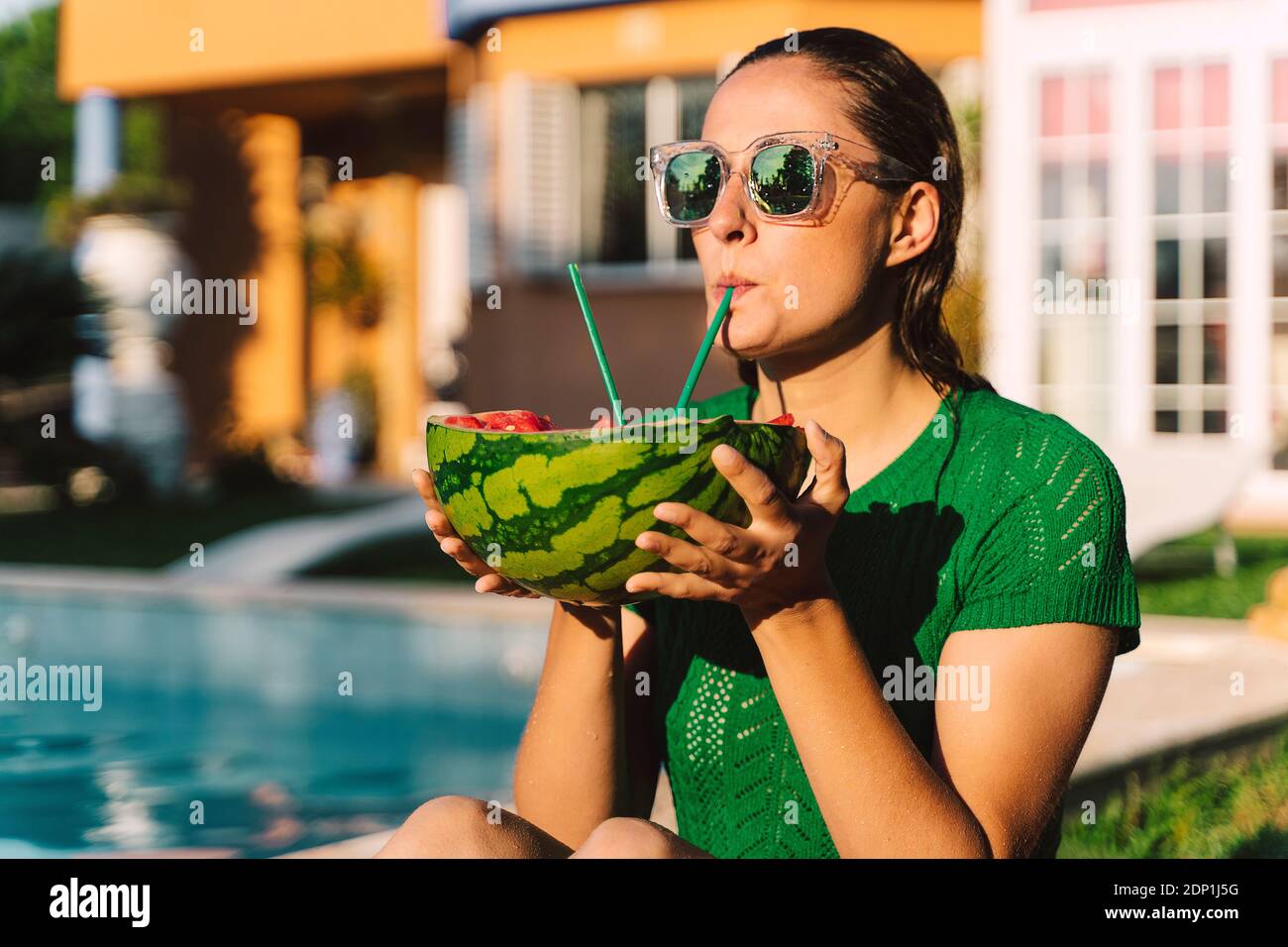 Frau trinkt mit den Pfoten von der Wassermelone am Pool Stockfoto