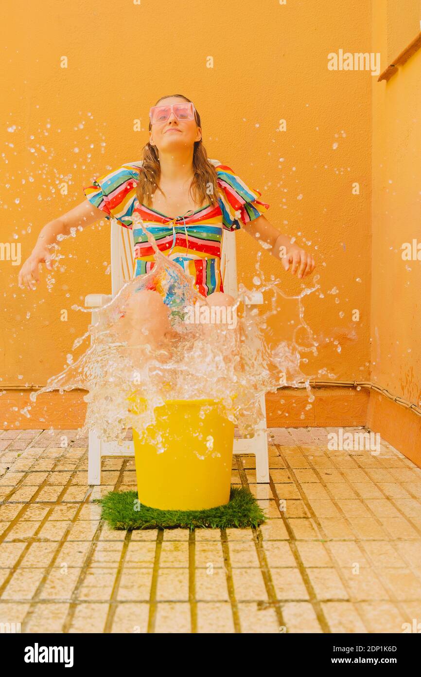 Porträt einer Frau auf einem Plastikstuhl sitzend, der mit Wasser spritzt Stockfoto