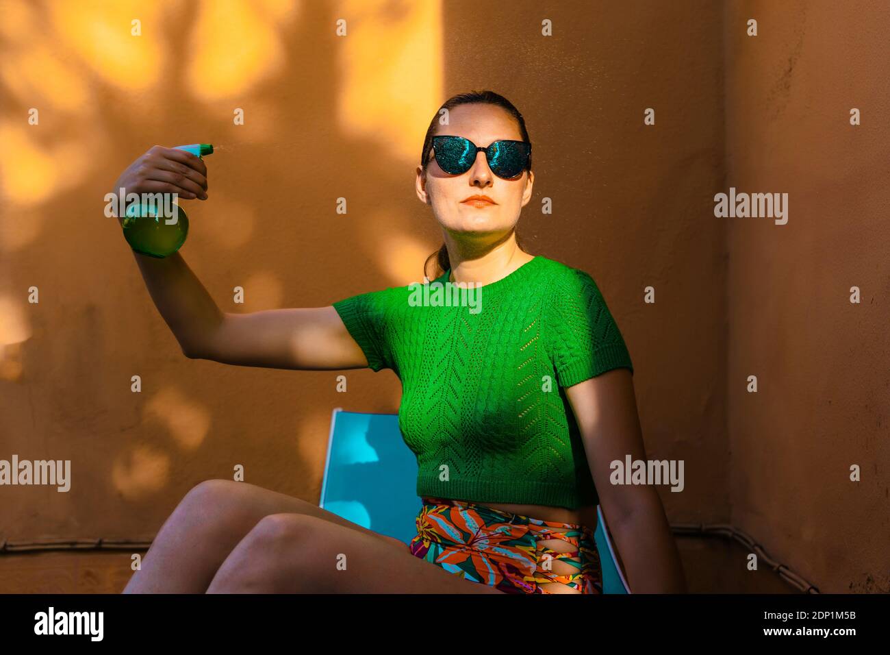 Frau in bunten Beachwear sitzen im Hinterhof, hält Sprühflasche Stockfoto