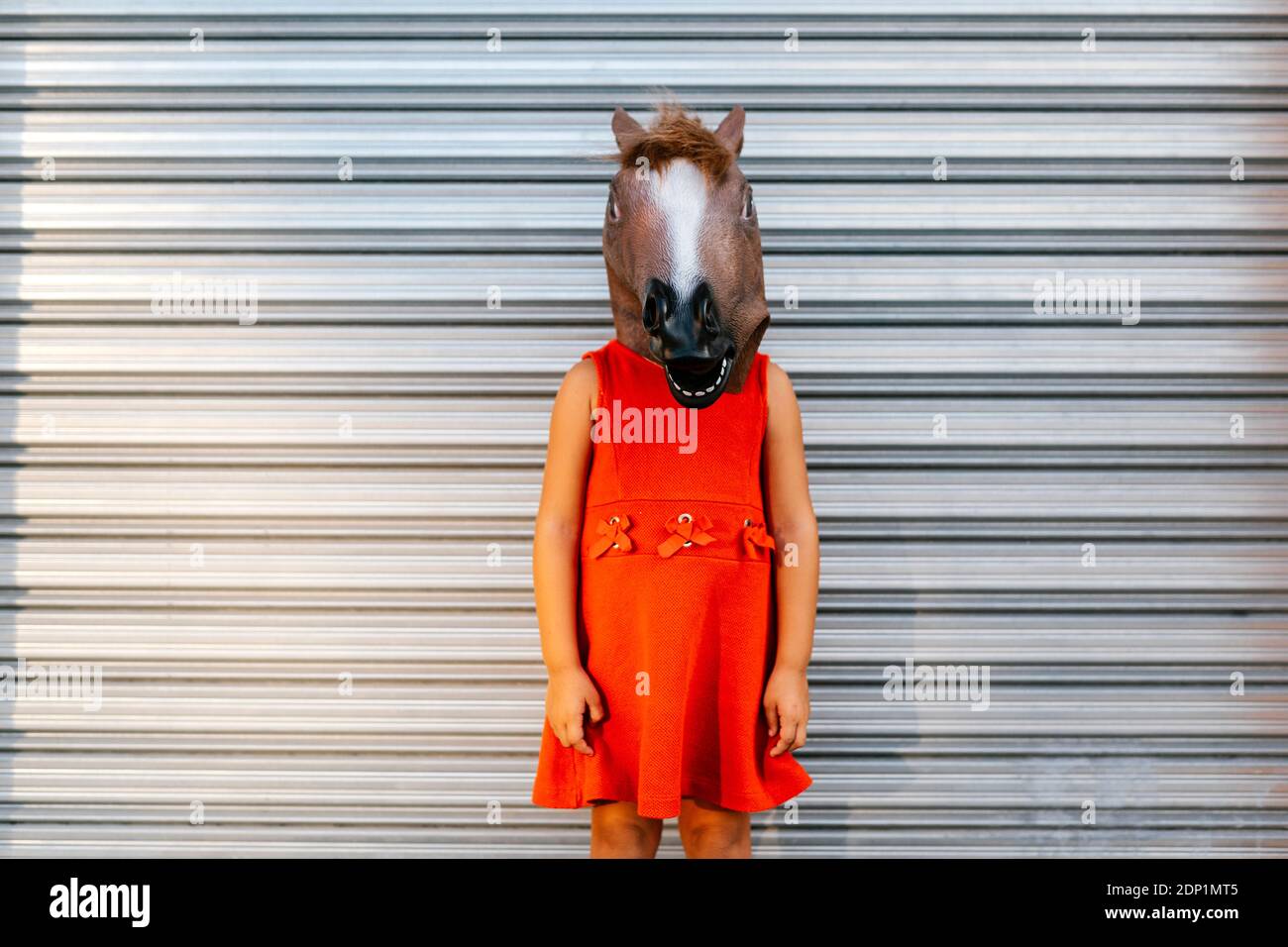 Kleines Mädchen mit einem Pferdekopf und einem roten Kleid Vor dem Metallverschluss Stockfoto