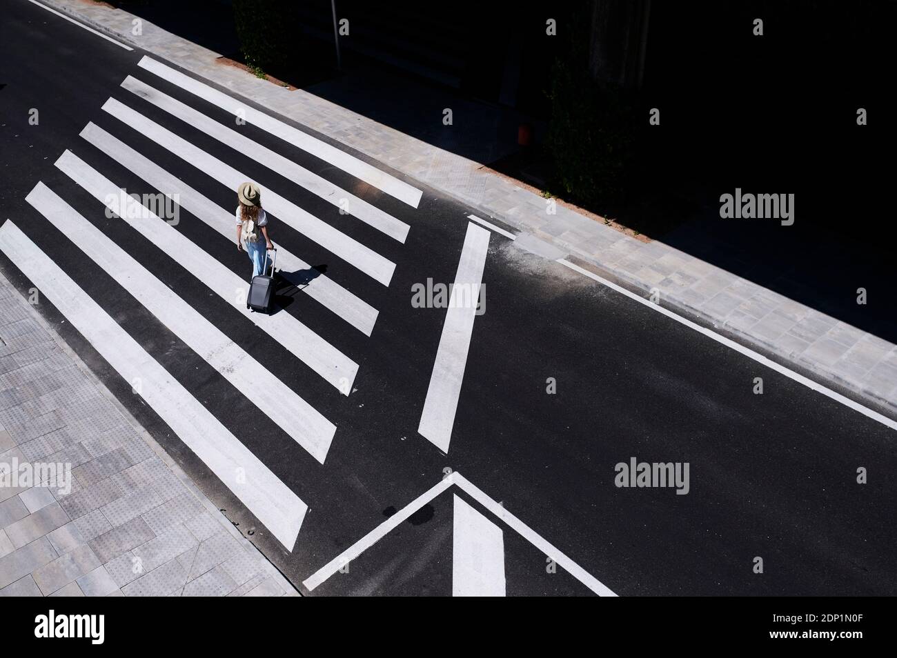 Blick von oben auf die junge Frau mit Gepäck überqueren einer Straße am Flughafen Stockfoto