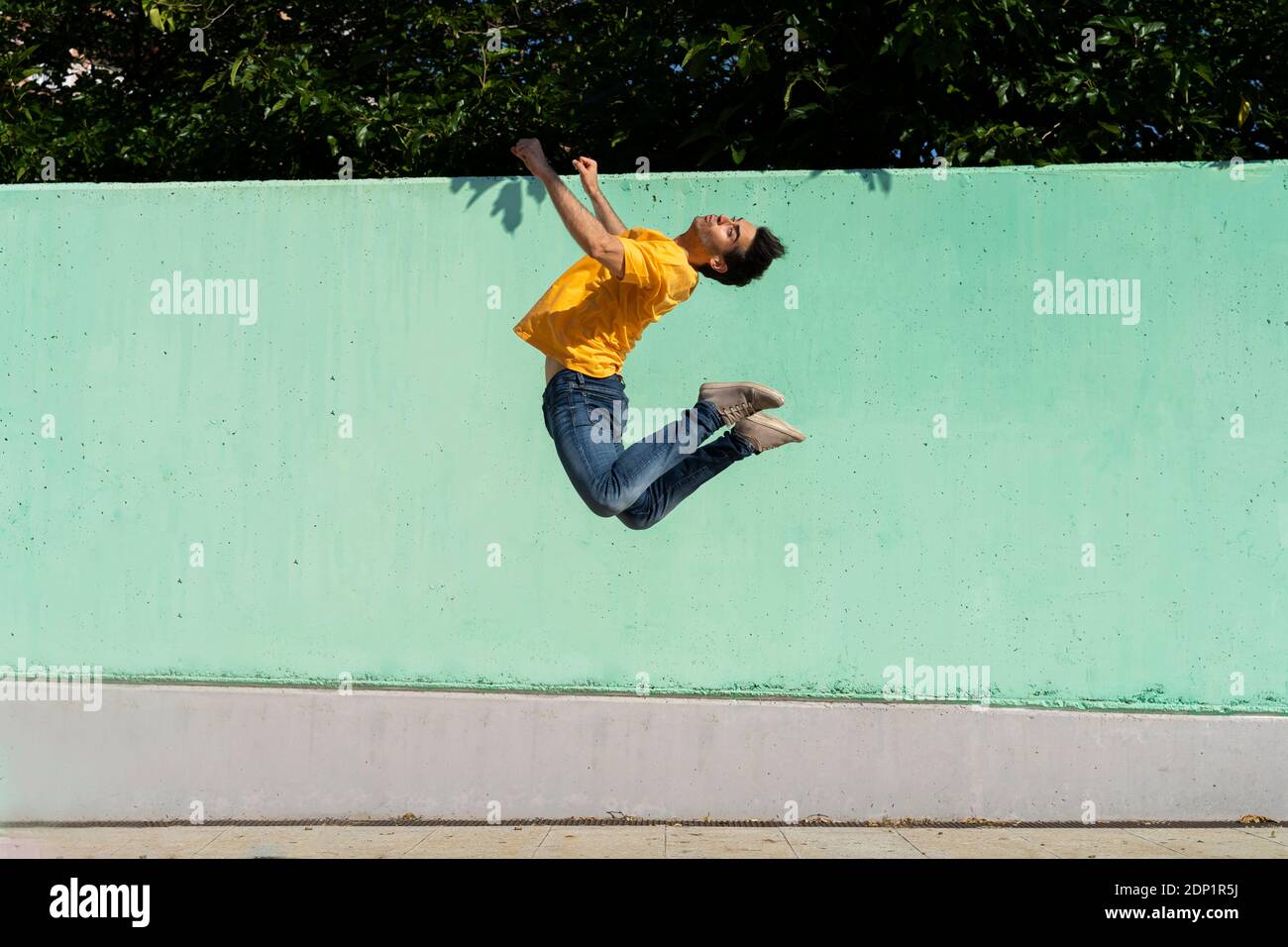 Mann springt mitten in der Luft vor der grünen Wand Stockfoto