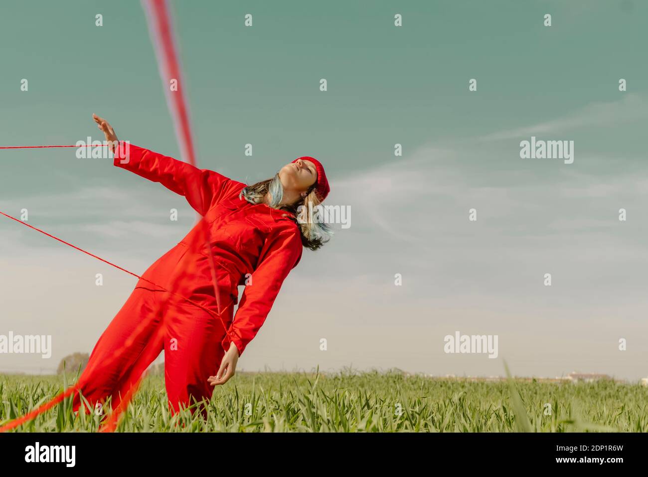 Junge Frau trägt roten Overall und Hut auf einem Feld mit roter Zeichenfolge Stockfoto