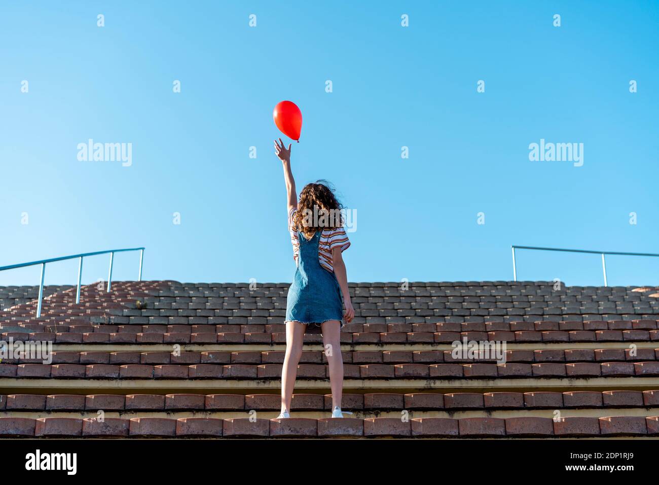 Junge Frau steht auf Tribünen, Loslassen von einem roten Ballon Stockfoto