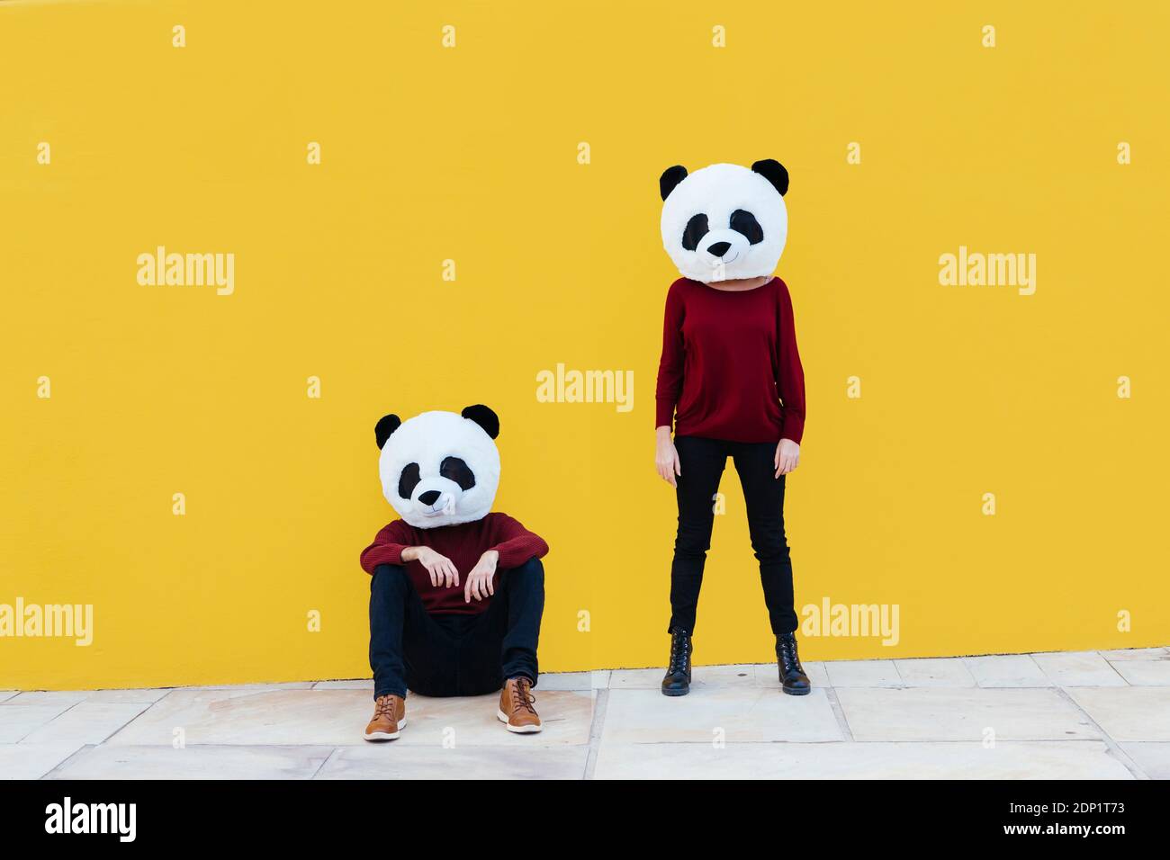 Männliche und weibliche Freunde in Panda Maske gegen gelbe Wand Stockfoto