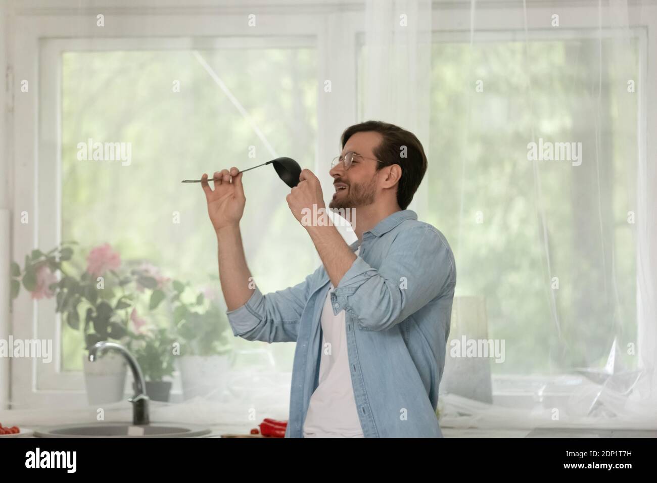 Fröhlicher junger Mann, der in der Küche tanzt und Lieblingslied singt Stockfoto