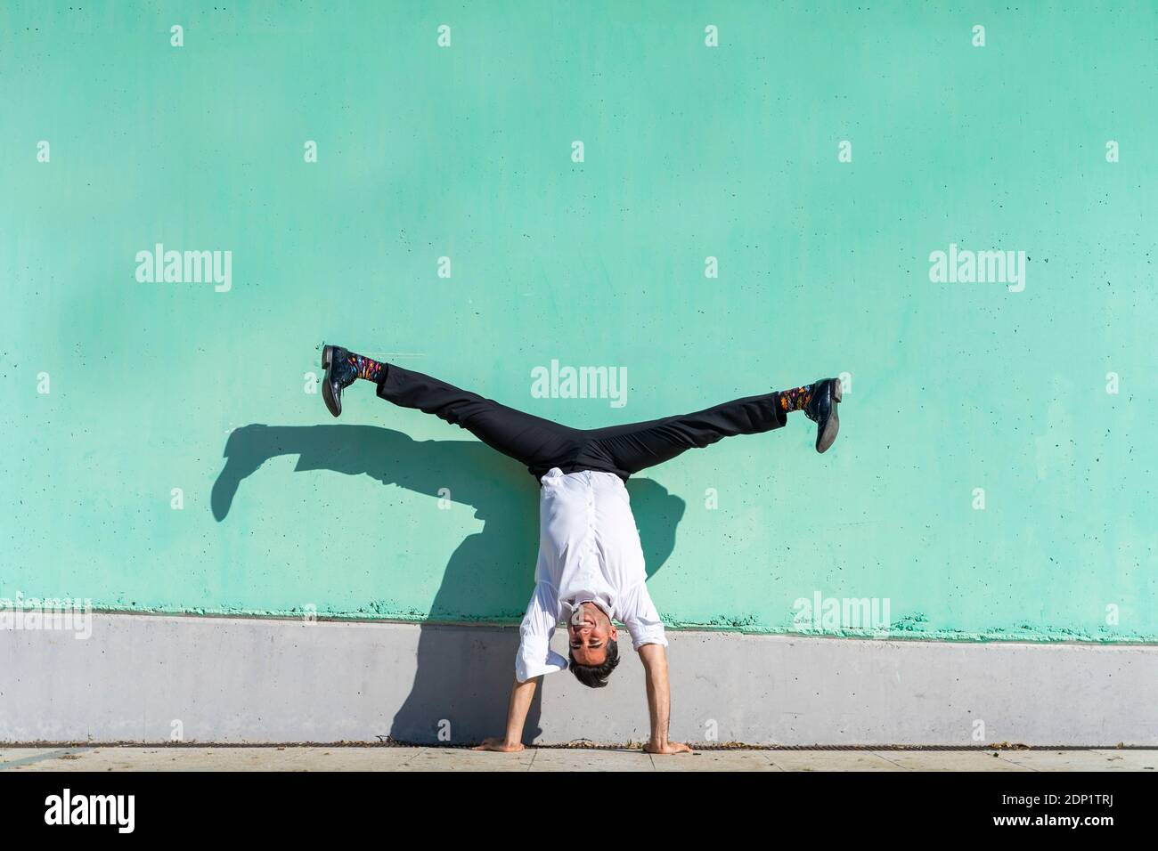 Geschäftsmann tut straddle Handstand gegen grüne Wand Stockfoto